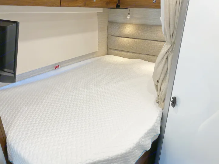 Comfortable rv rental sleeping area with a fresh white bed, cushioned headboard, and emergency exit.. Winnebago View 2022