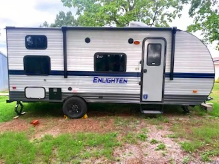 This modern silver travel trailer, an ideal RV rental, is parked on grass, ready for your next camping adventure.. Gulf Stream Enlighten 2022