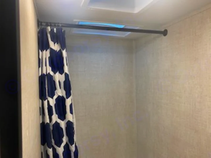 Inside an RV rental: a compact shower with a patterned blue & white curtain and tension rod, featuring a ceiling vent.. Gulf Stream Enlighten 2022