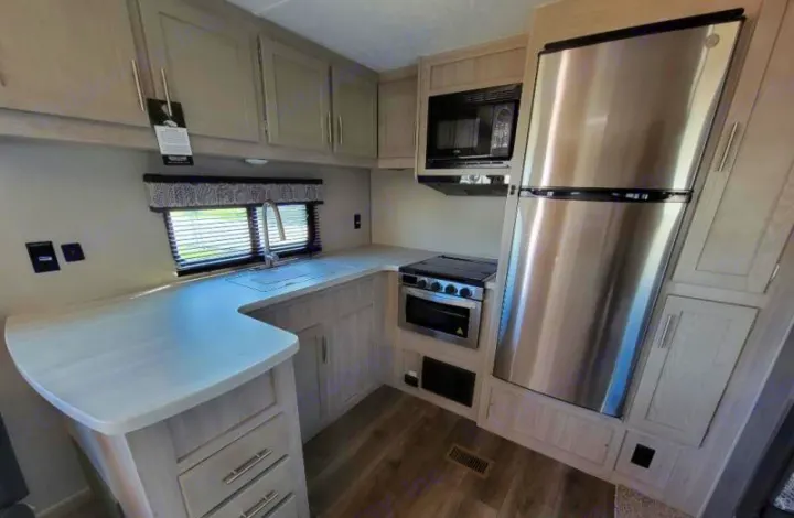 Modern RV rental kitchen with stainless fridge, stove, microwave, and sink. Light wood-look cabinets and flooring.. Forest River Coachmen Catalina Legacy 2022