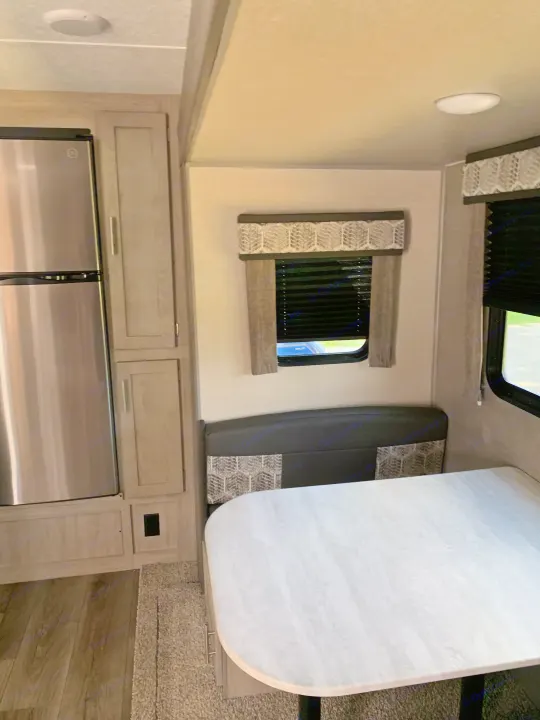 RV rental interior: modern dining booth, light wood cabinets, and stainless steel refrigerator in a well-lit space.. Forest River Coachmen Catalina Legacy 2022