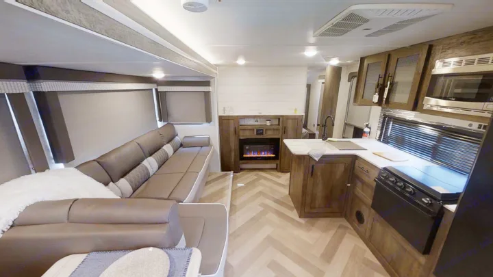 Modern RV rental interior with a comfortable sofa, full kitchen, electric fireplace, and stylish herringbone floor. Perfect for adventures.. Forest River Wildwood X-Lite 2022