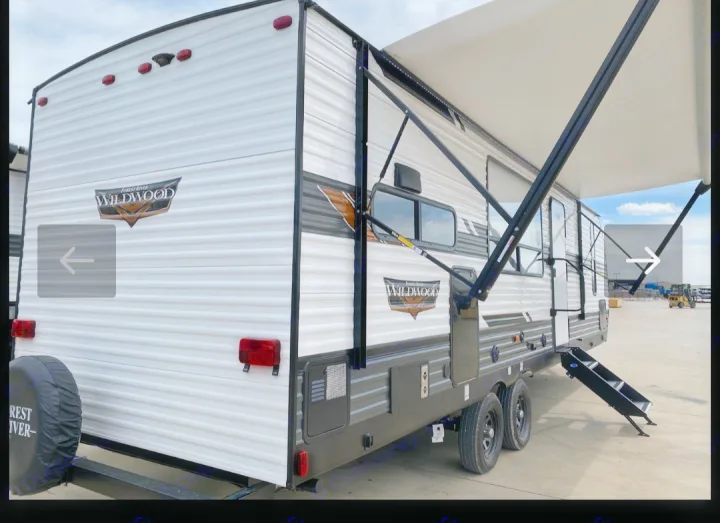 A modern white and grey RV with an extended awning and deployed steps, ready for rv rental adventures. Features rear spare tire.. Forest River Wildwood X-Lite 2022