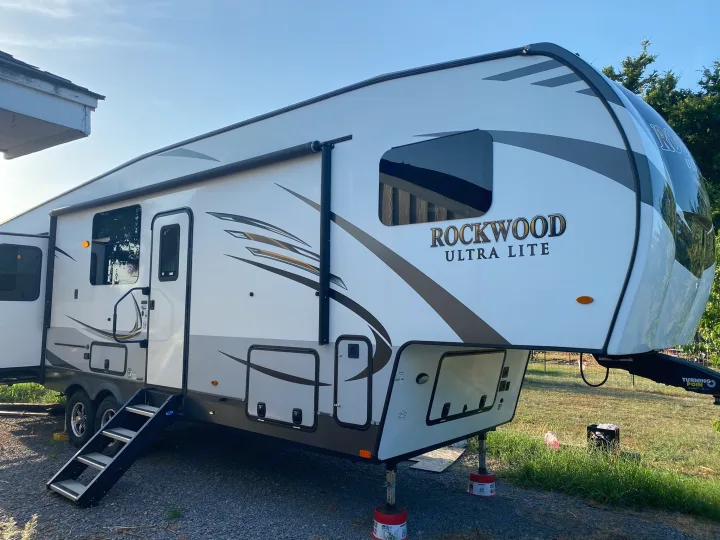 A large white Rockwood Ultra Lite fifth-wheel RV with steps down, parked on gravel. Consider this for your RV rental!. Forest River Rockwood Ultra Lite 2020