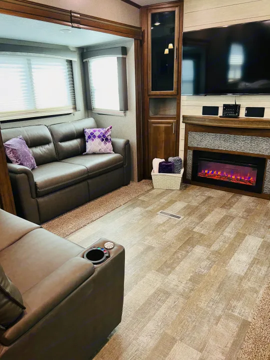 Modern RV rental living area with brown sofas, purple pillows, electric fireplace, TV, and light wood-look floor.. Forest River Rockwood Ultra Lite 2020