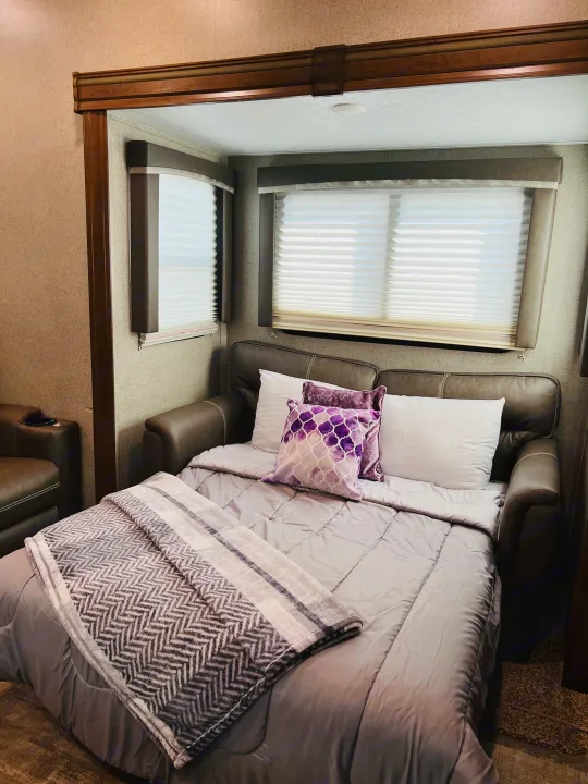 Experience comfort in our RV rental: a plush sofa bed with purple pillows and cozy blankets, perfect for your journey.. Forest River Rockwood Ultra Lite 2020