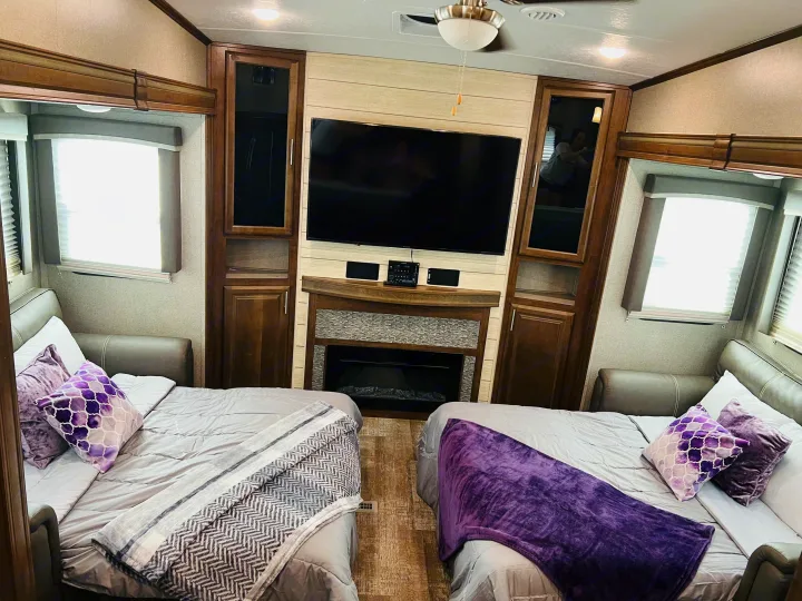 Cozy RV rental interior with two beds, a central TV, and electric fireplace, creating a comfortable living space.. Forest River Rockwood Ultra Lite 2020