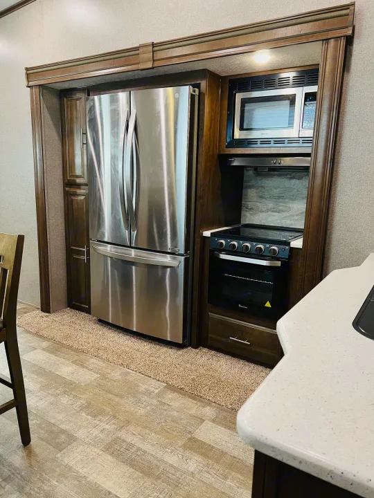 Spacious RV rental kitchen featuring a large stainless steel LG fridge, built-in microwave, oven, and dark wood cabinetry.. Forest River Rockwood Ultra Lite 2020
