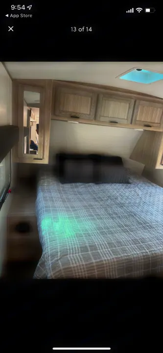 Modern RV rental bedroom: cozy bed with plaid comforter, light wood overhead cabinets, and convenient side storage.. Shadow Trailers 277bhs 2022
