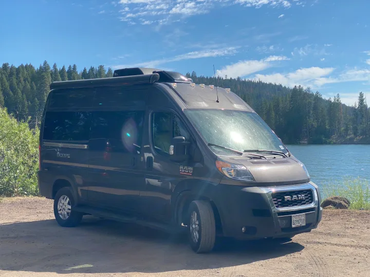 RV rental camper van parked by a serene lake with a forest background. Ready for a nature adventure.. Thor Motor Coach Scope 2022
