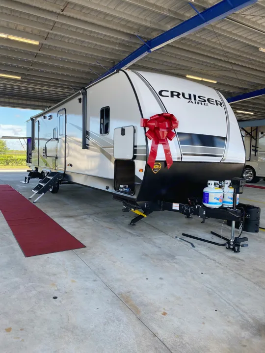 A pristine white Cruiser Aire travel trailer, adorned with a large red bow, sits in a showroom,. Keystone RV Other 2021
