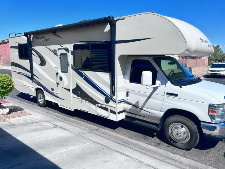 White Freedom Elite RV rental, a Class C motorhome, parked curb-side on a sunny day, ready for your road trip.. Thor Freedom Elite 2015