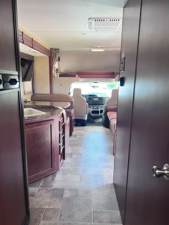 Looking forward into a spacious RV rental interior, showing the kitchen, dinette, cockpit, and overhead bunk.. Thor Freedom Elite 2015