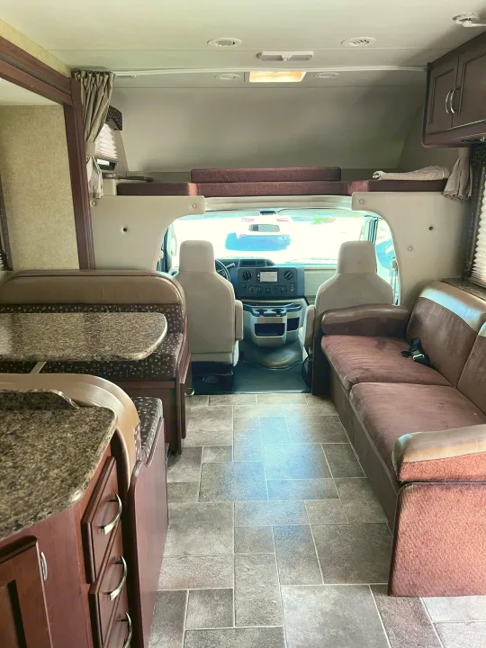 Spacious RV rental interior featuring a front cab, dinette, sofa, and overhead bunk. Perfect for road trip adventures.. Thor Freedom Elite 2015