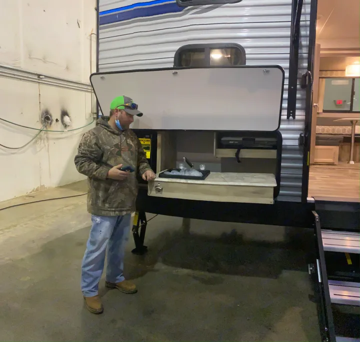 A man in a cap examines an RV rental with its convenient outdoor kitchen, featuring a sink and prep area.. Forest River Coachmen Catalina Legacy 2020