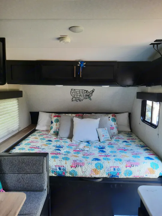 RV rental interior: a cozy bedroom with a patterned quilt, multiple pillows, dark cabinet, and small window, ideal for travel.. Forest River Cherokee Wolf Pup 2022