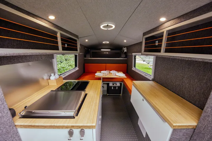 Modern RV rental interior: kitchen with bamboo counters, orange dining area, overhead storage, and rear bed.. Chevrolet silverado 2500 2022