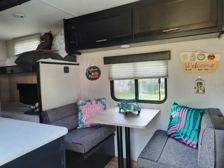 Inviting RV rental interior featuring a dinette with gray seating, a central table, window, and visible bed area. Compact and homey.. Forest River Cherokee Wolf Pup 2022