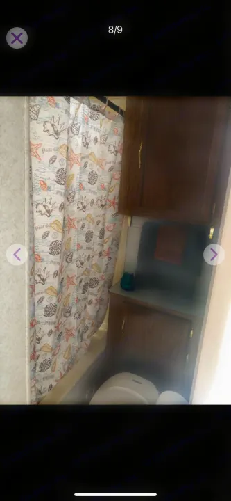 RV rental bathroom featuring a small shower/tub with a seashell-patterned curtain, toilet, and wooden storage cabinets with towels.. Shasta Flite 2000