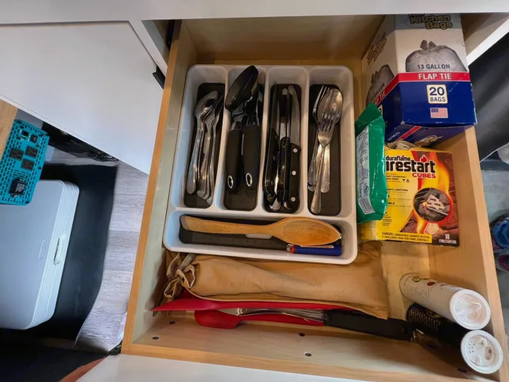 Organized RV rental kitchen drawer with cutlery, firestarters, trash bags, and various cooking supplies.. Ford Econoline E350 Extended 2004