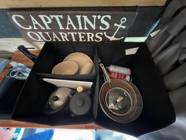 RV rental kitchen setup with 'Captain's Quarters' sign. Organized storage bins hold plates, pans, kettle, & butane fuel.. Ford Econoline E350 Extended 2004