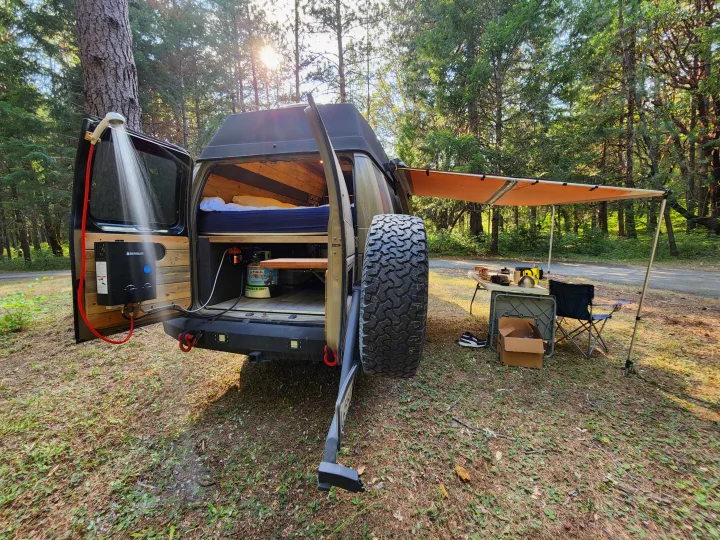 Explore nature with this unique RV rental, featuring an outdoor shower, cozy bed, and an awning for comfortable campsite living.. Ford Econoline E350 Extended 2004