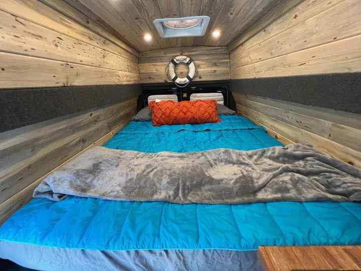 Cozy campervan bed in an RV rental, featuring rustic wooden walls, a bright blue comforter, and nautical decor.. Ford Econoline E350 Extended 2004