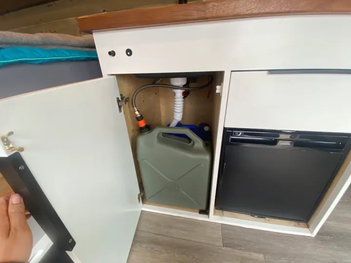 Compact camper kitchen in an RV rental, showing a gray water tank connected to a sink drain and a Dometic fridge.. Ford Econoline E350 Extended 2004