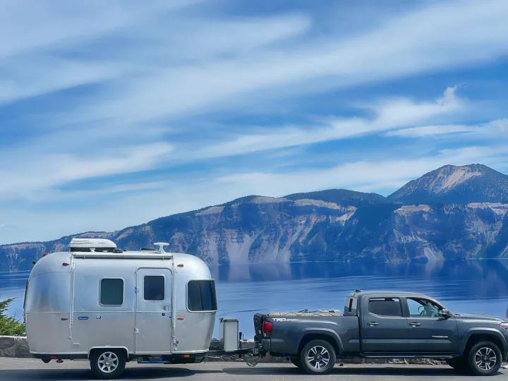 Silver Airstream travel trailer (RV rental) with truck by Crater Lake & mountains. Great for trips!. Airstream Bambi 2022