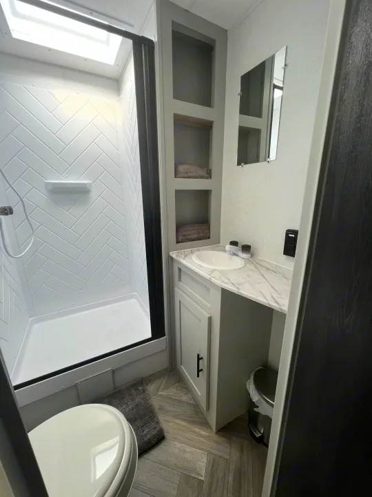 Modern RV rental bathroom with a compact shower, toilet, and vanity. Features white herringbone tiling and wood-look floors.. Forest River Salem FSX 270RTKX 2022