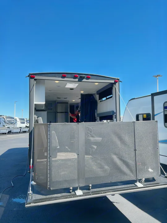 An RV rental's ramp opens to a screened patio deck. A person is inside the bright camper on a clear day.. Forest River Salem FSX 270RTKX 2022