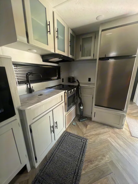 Modern RV rental kitchen featuring light cabinets, stainless steel fridge, and a stylish herringbone floor.. Forest River Salem FSX 270RTKX 2022
