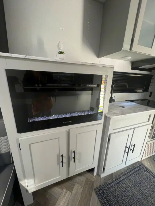 RV rental interior featuring a Furrion electric fireplace below a "TV BACKER" wall, plus a kitchen with sink.. Forest River Salem FSX 270RTKX 2022