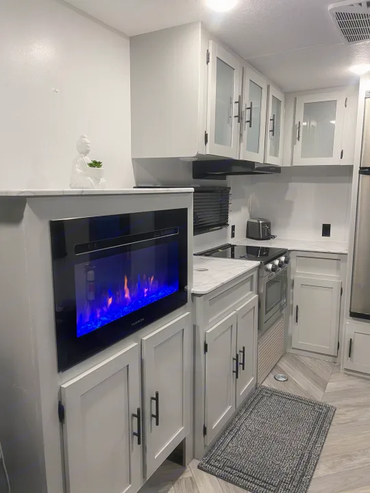 Modern RV rental interior: well-equipped kitchen with electric fireplace, sleek cabinets, and cozy rug.. Forest River Salem FSX 270RTKX 2022