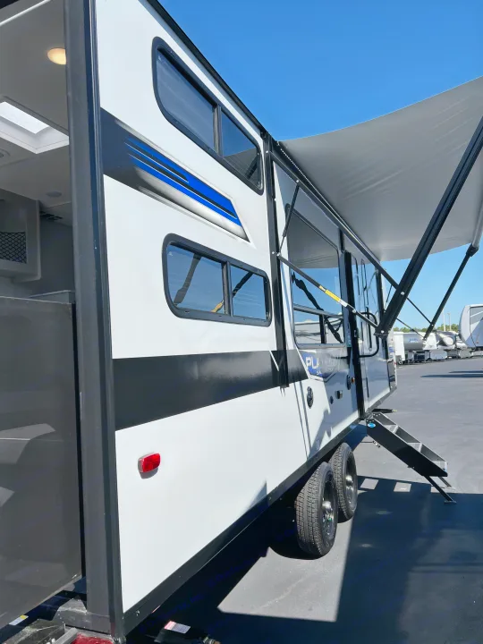 Modern white RV rental travel trailer with black/blue accents, extended awning, and steps deployed under clear sky.. Forest River Salem FSX 270RTKX 2022