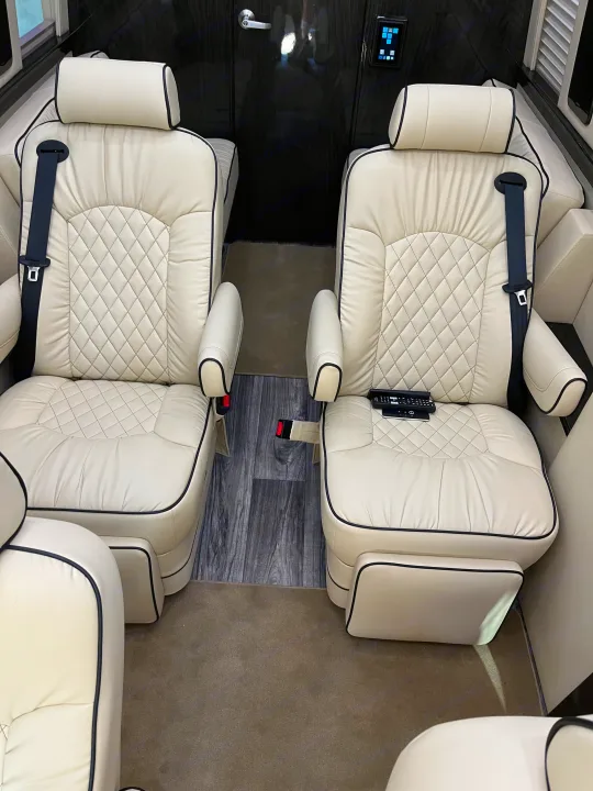 Inside a luxury RV rental, featuring two comfortable cream leather captain's chairs with diamond-quilted upholstery.. Midwest Automotive Designs Midwest Automotive Designs Class B 2021