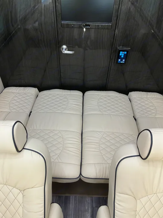 Luxurious RV rental interior featuring cream quilted leather beds, dark wood walls, and an entertainment screen.. Midwest Automotive Designs Midwest Automotive Designs Class B 2021