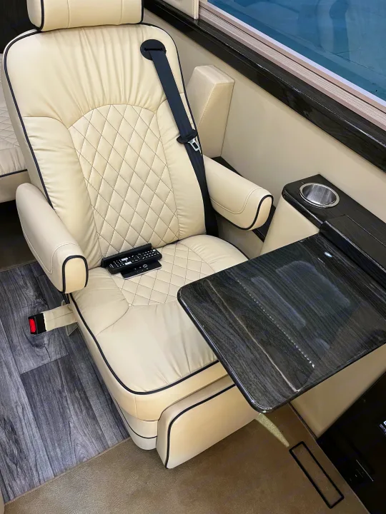 Plush cream captain's chair with seatbelt, remotes, and glossy table with cupholder, showcasing a premium RV rental interior.. Midwest Automotive Designs Midwest Automotive Designs Class B 2021