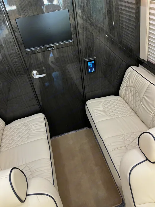 Plush RV rental cabin: cream quilted leather seating, dark wood-grain walls, built-in display, smart controls.. Midwest Automotive Designs Midwest Automotive Designs Class B 2021