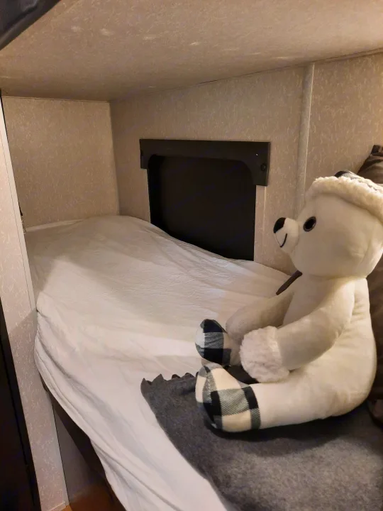 RV rental interior: A white stuffed animal rests on the bed next to a dark, built-in storage cubby.. Forest River Cherokee Wolf Pup 2022