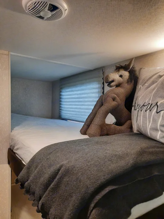 RV rental bedroom interior: A bed with a plush horse toy, window blinds, and an overhead vent in a compact living space.. Forest River Cherokee Wolf Pup 2022