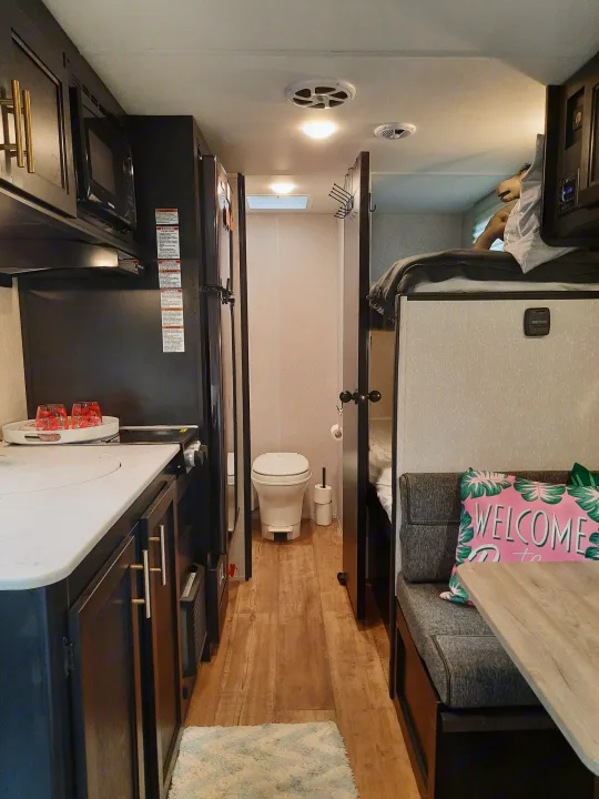 Inside an RV rental: cozy bedroom, compact kitchen with stovetop, dining booth, and small bath with toilet. Modern interior.. Forest River Cherokee Wolf Pup 2022