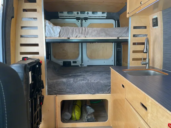 Custom camper van RV rental interior featuring two bunk beds, a compact kitchen with sink, and under-bed storage.. RAM ProMaster 2022