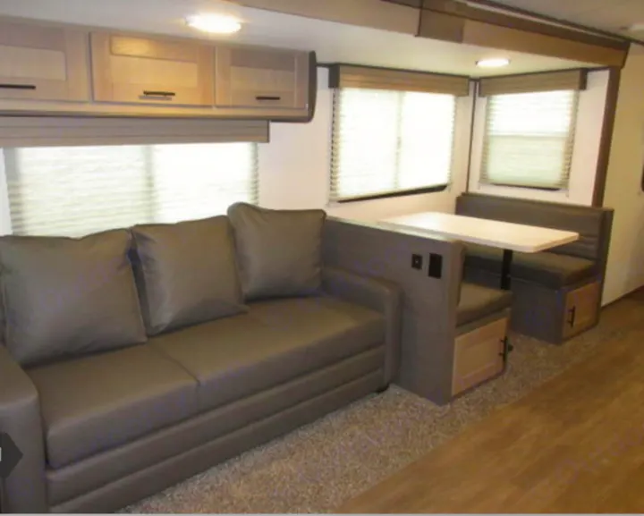 RV rental interior: living area with a sofa, transitioning to a dinette with bench seating and windows.. Cruiser RV Shadow Cruiser 2022