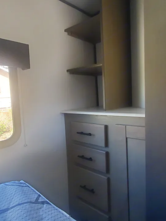 RV rental bedroom featuring a built-in dresser with drawers, open shelves, and a window for comfortable living.. Cruiser RV Shadow Cruiser 2022