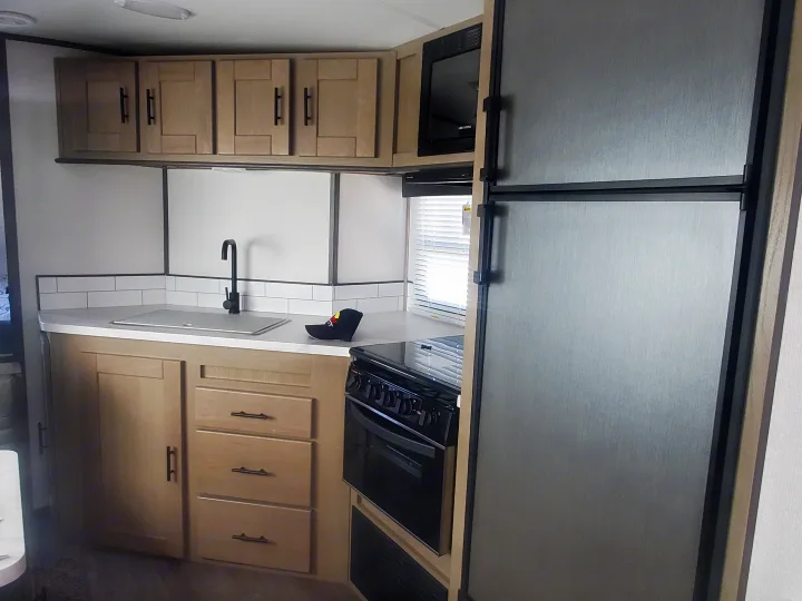 RV rental kitchen: light wood cabinets, stainless steel fridge, black oven, microwave, and sink.. Cruiser RV Shadow Cruiser 2022