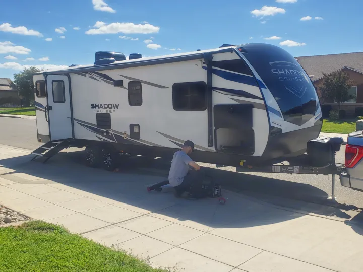 A man prepares a white and blue Shadow Cruiser travel trailer, possibly for an RV rental adventure.. Cruiser RV Shadow Cruiser 2022