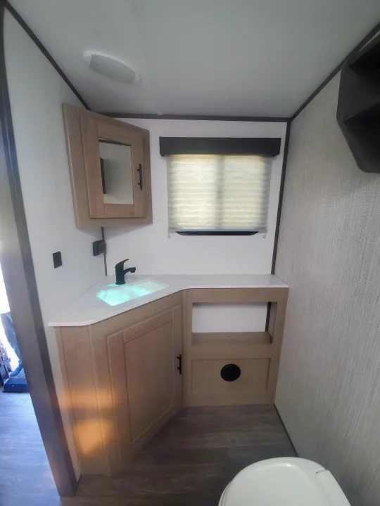Modern RV rental bathroom interior featuring a compact corner vanity, illuminated sink, toilet, and window.. Cruiser RV Shadow Cruiser 2022