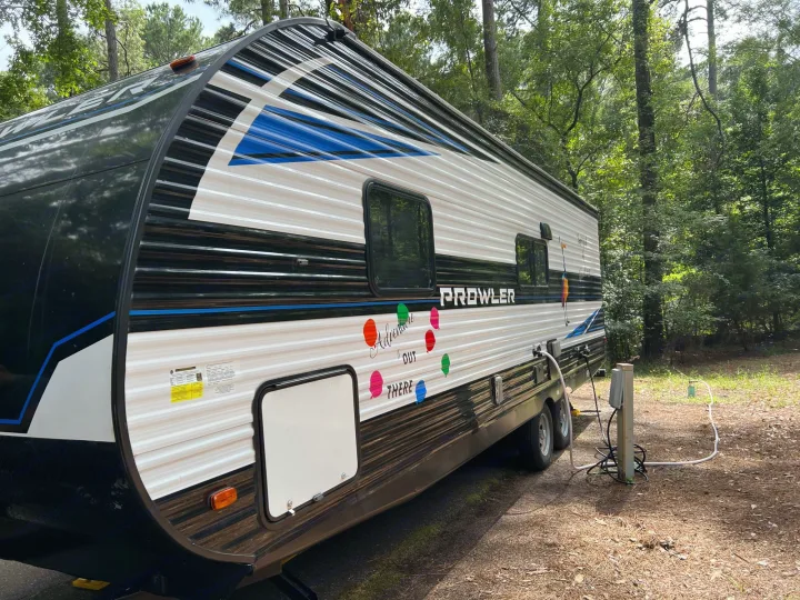 Prowler travel trailer RV rental set up at a wooded campsite with utility hookups, ready for adventure.. Heartland Prowler 2021