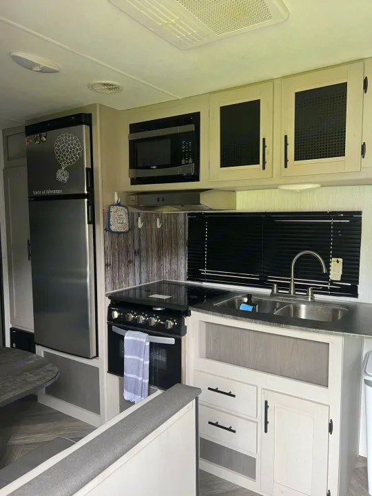 Modern RV rental kitchen interior with fridge, microwave, stove, sink, light cabinets, and dinette seating.. Heartland Prowler 2021